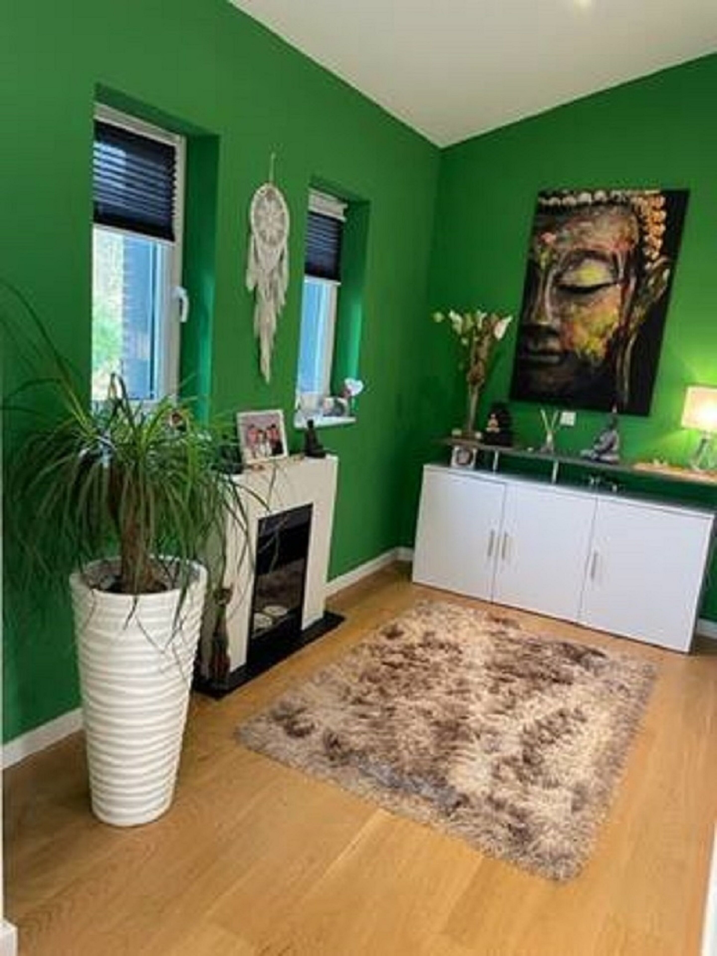 A room with green walls, a white cabinet, a large painting, a potted plant, and a rug.