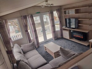 A cozy living room with a sofa, a TV, and a fireplace. - Bluebell corner - with small enclosed decking (Hastings)