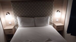 A neatly made bed with two pillows, a bedside table with a lamp, and a patterned headboard.