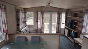 A cozy room with a glass table and chairs, a sofa, a TV, and a balcony with curtains.