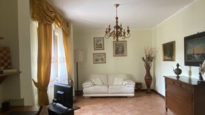 A living room with a sofa, a TV, a chandelier, and a dining area with a table and chairs. - "COTTAGE ULIVO" 
Codice Identificativo: 046017LTN2254 (Lucca)