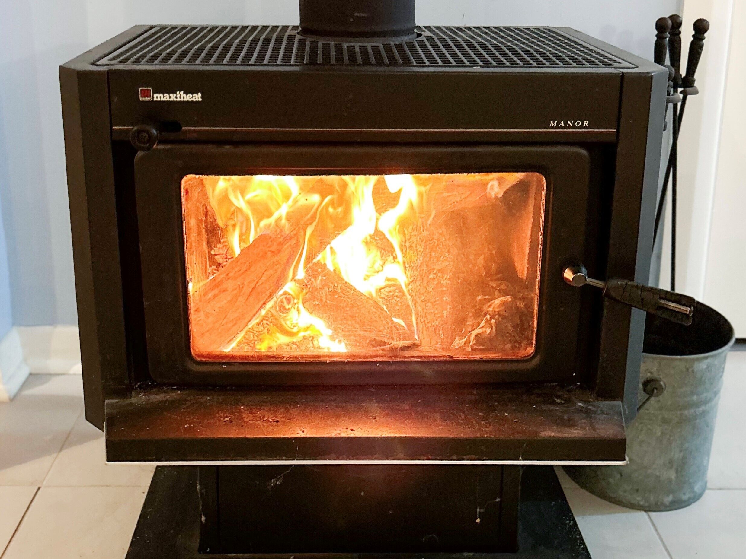 A wood-burning stove with visible flames, a control knob, and a metal bucket nearby.