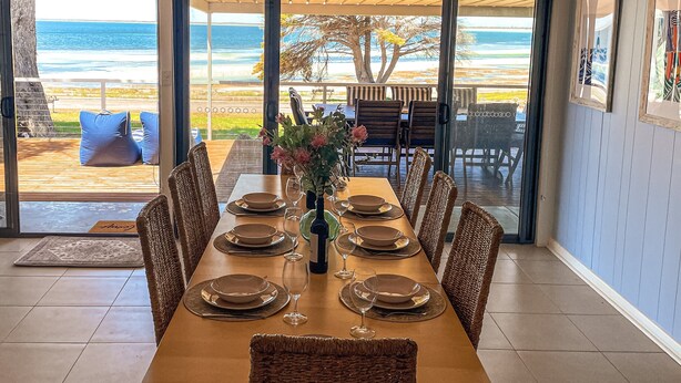 Un espace repas offrant une vue sur l’océan, une table en bois dressée pour six personnes, des chaises en osier et une cloison en verre.