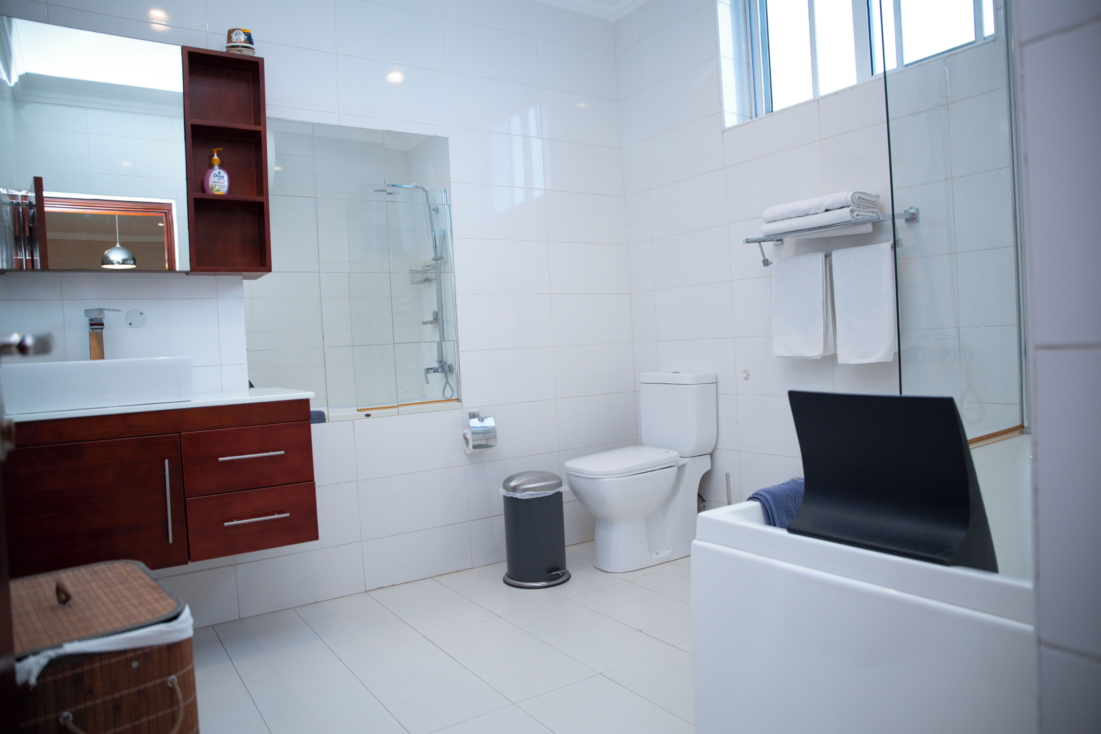 A modern bathroom with a white sink, wooden vanity, glass shower enclosure, white toilet, and a bathtub with a towel rack.