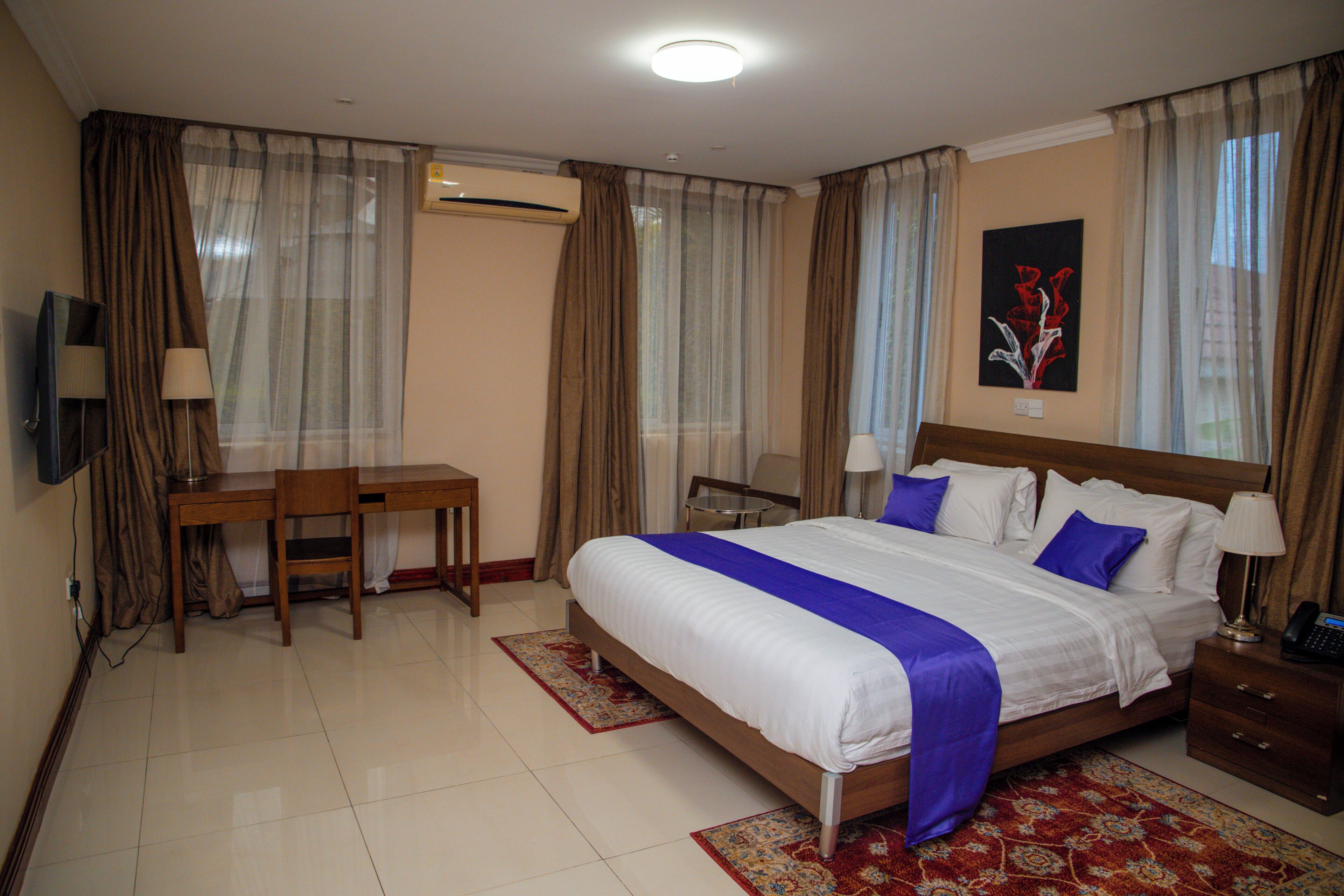 A hotel room with a bed, a desk, a chair, a TV, and a nightstand.
