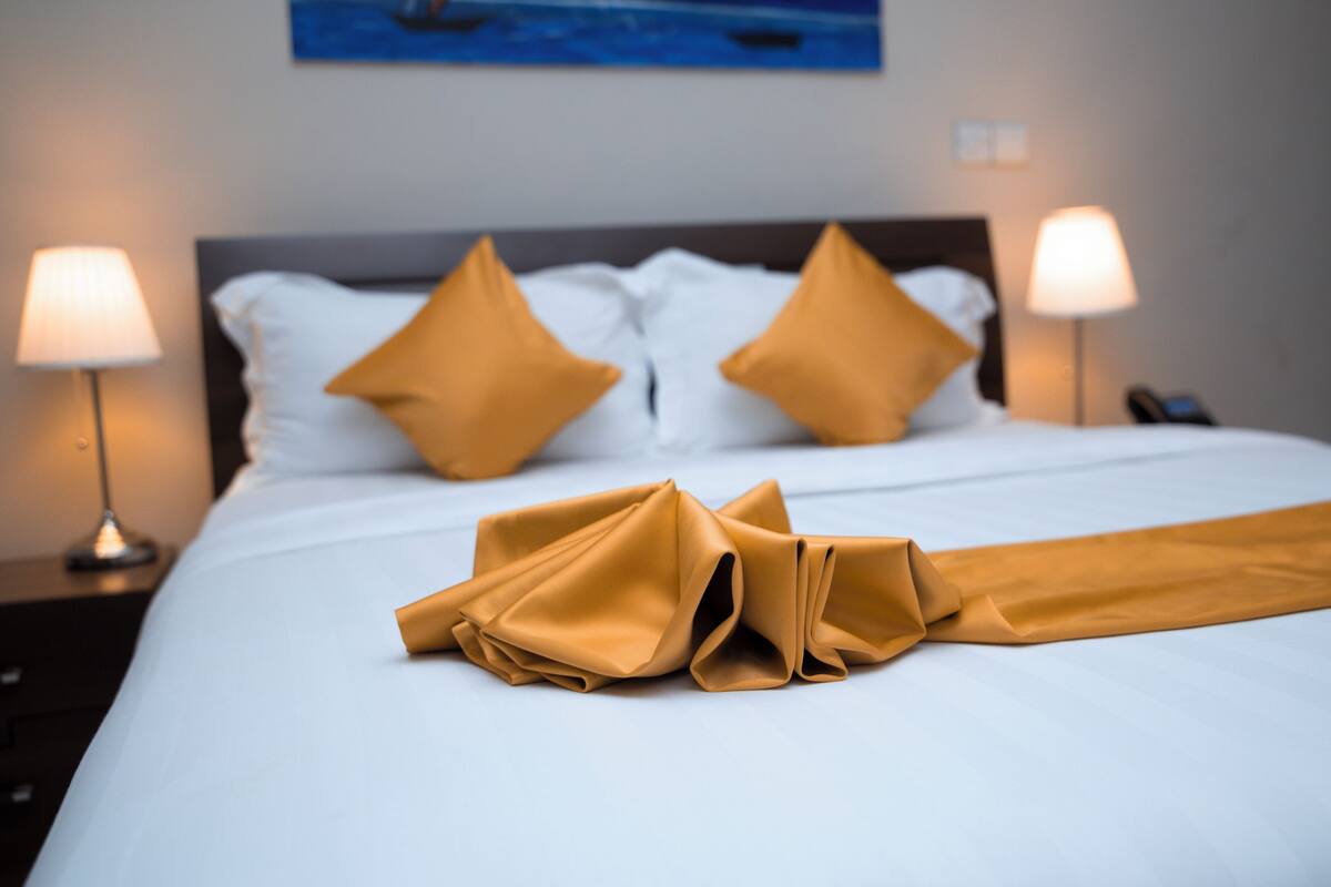 A neatly made bed with white linens and two yellow pillows, flanked by two bedside lamps.