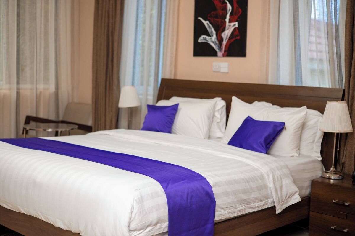 A hotel room with a large bed, two bedside tables, a nightstand, and a painting on the wall.