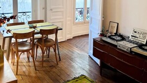 Una habitación con una mesa de comedor y sillas, piso de madera, alfombra verde y un equipo de música.