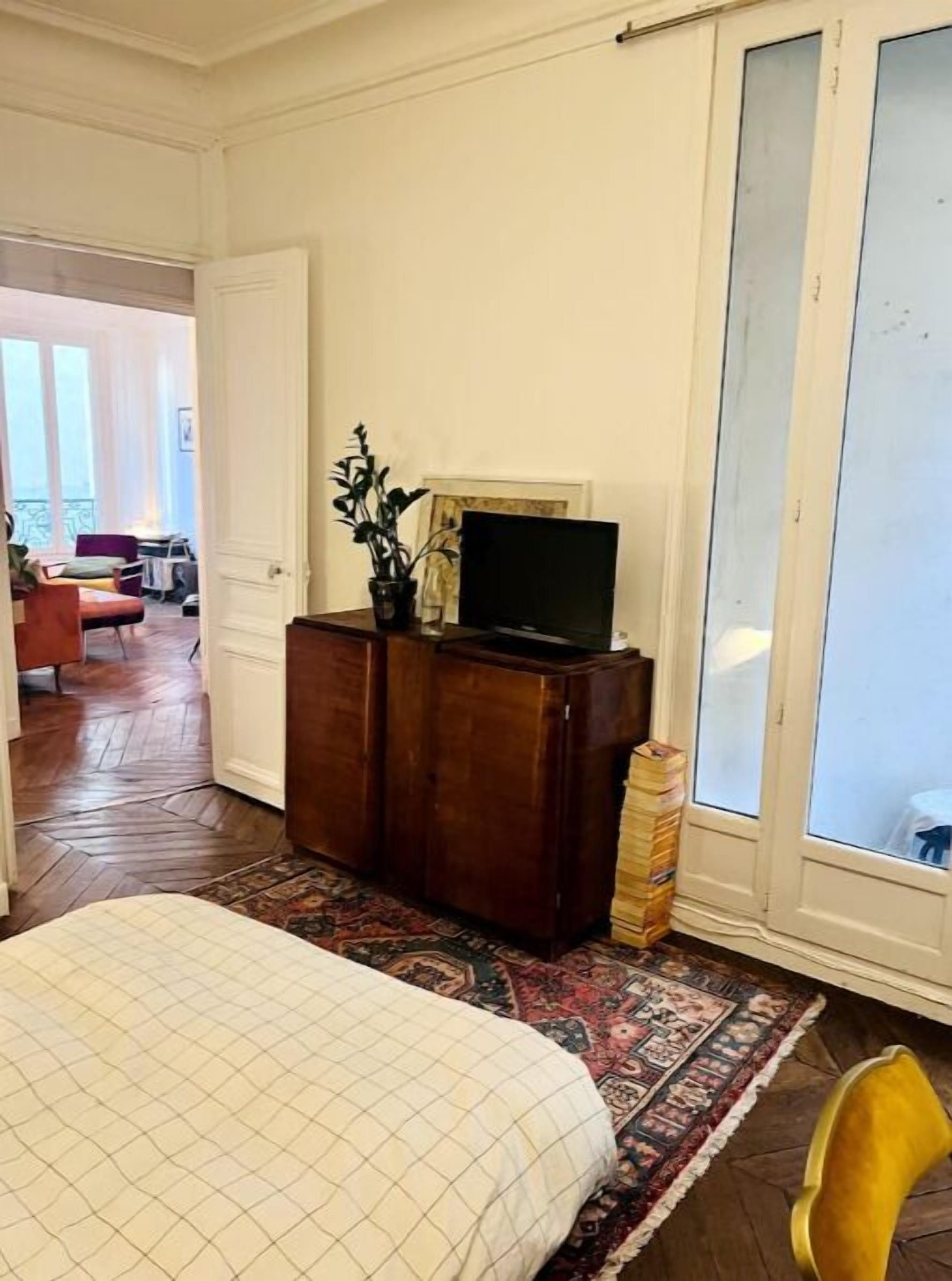 Une chambre à coucher avec un lit, une commode en bois, un téléviseur et une grande fenêtre.