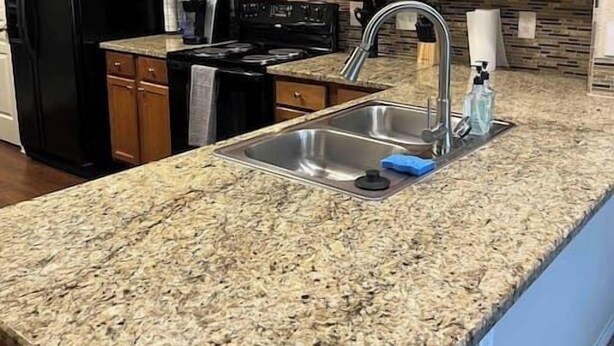 A kitchen with granite countertops, a stainless steel sink, wooden cabinets, a black refrigerator, a microwave, and a stove. - Hill Country Hiatus! (Bee Cave)