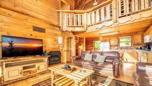 A wooden cabin interior with a TV, leather sofa, and a dining area.