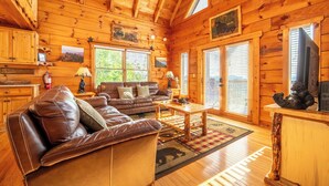 A wooden cabin interior with a leather couch, wooden coffee table, and a television on a wooden stand.