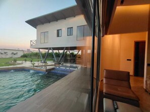 A modern house with a swimming pool, a balcony, and a chair. - Shaw Estate_Cottage151A (Noida)