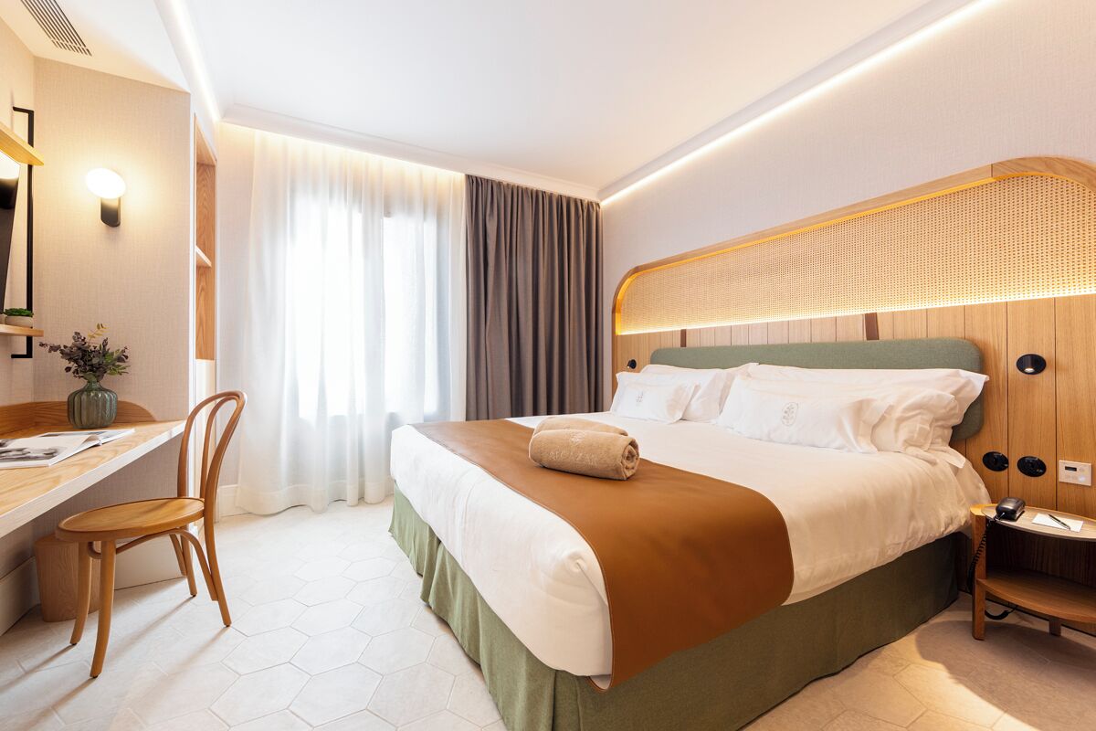 A modern hotel room with a large bed, a desk, and a chair.