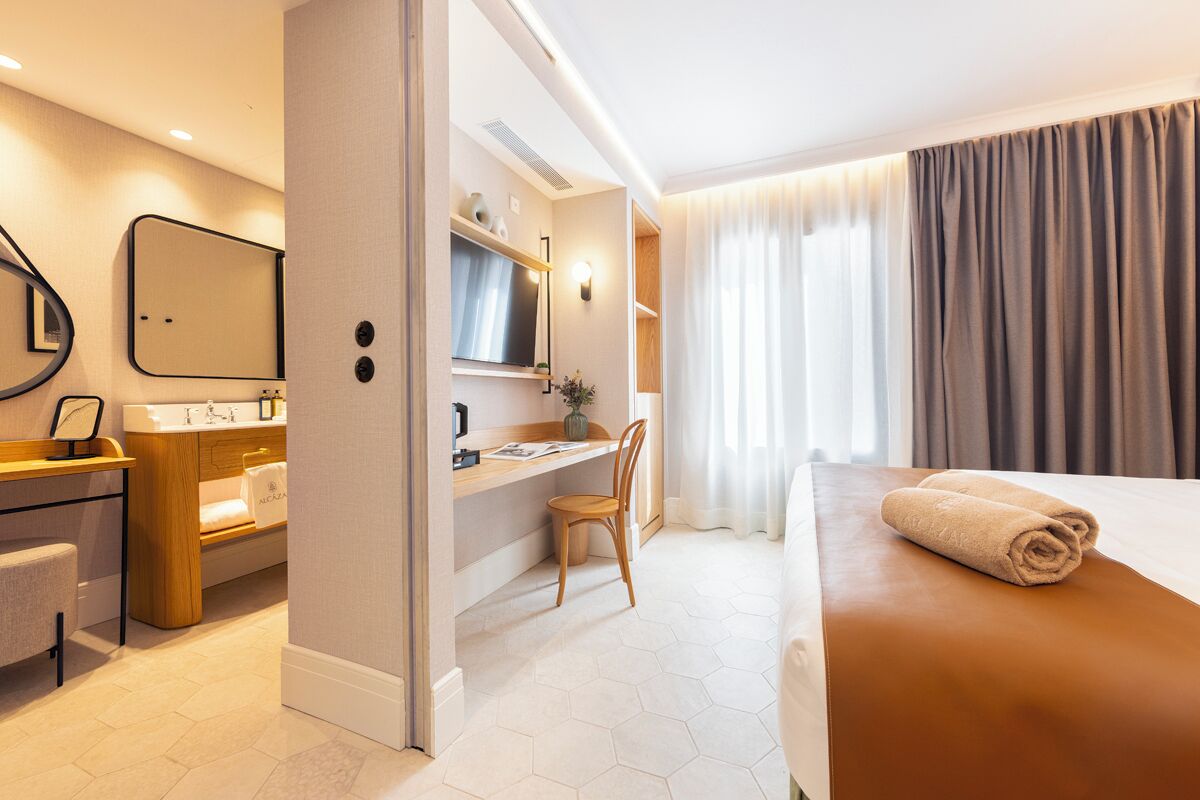 Una camera d'albergo moderna con un letto, una scrivania, una sedia, un tavolino da trucco con uno specchio e una finestra con tende.