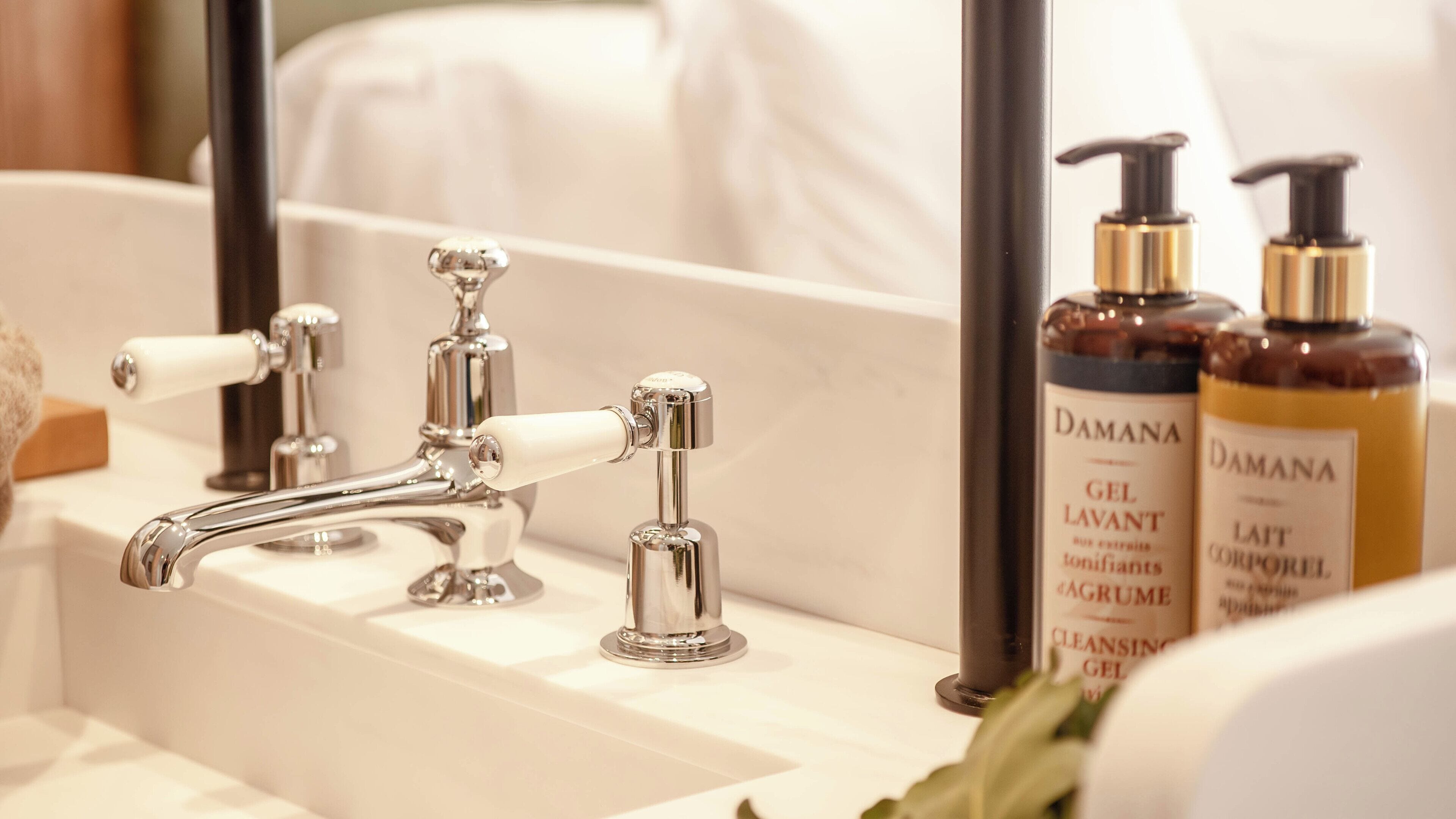 A bathroom with a white sink, chrome faucet, and two bottles of Damana gel.