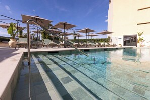 Una piscina con agua cristalina, rodeada de sillas de descanso y sombrillas, con un edificio al fondo.