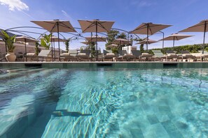 En klar swimmingpool med liggestole og parasoller.