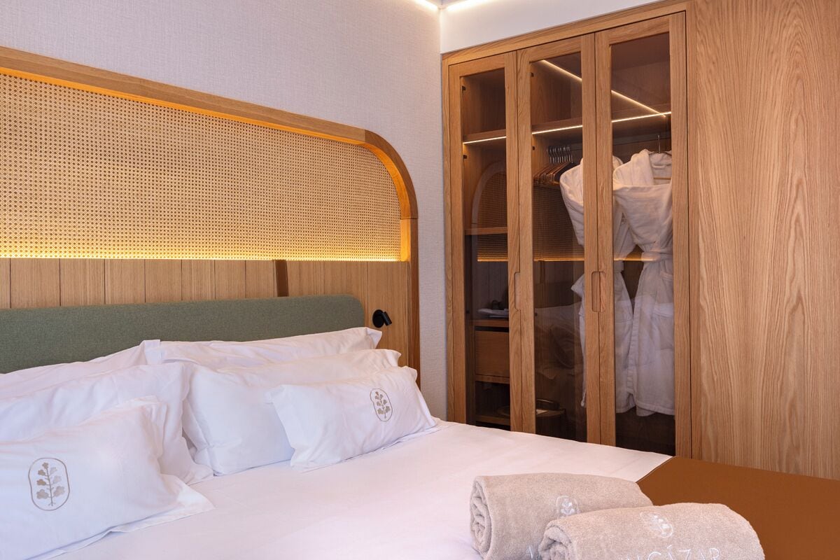 Quarto de hotel com cama, guarda-roupa de madeira e cabeceira com padrão trançado.