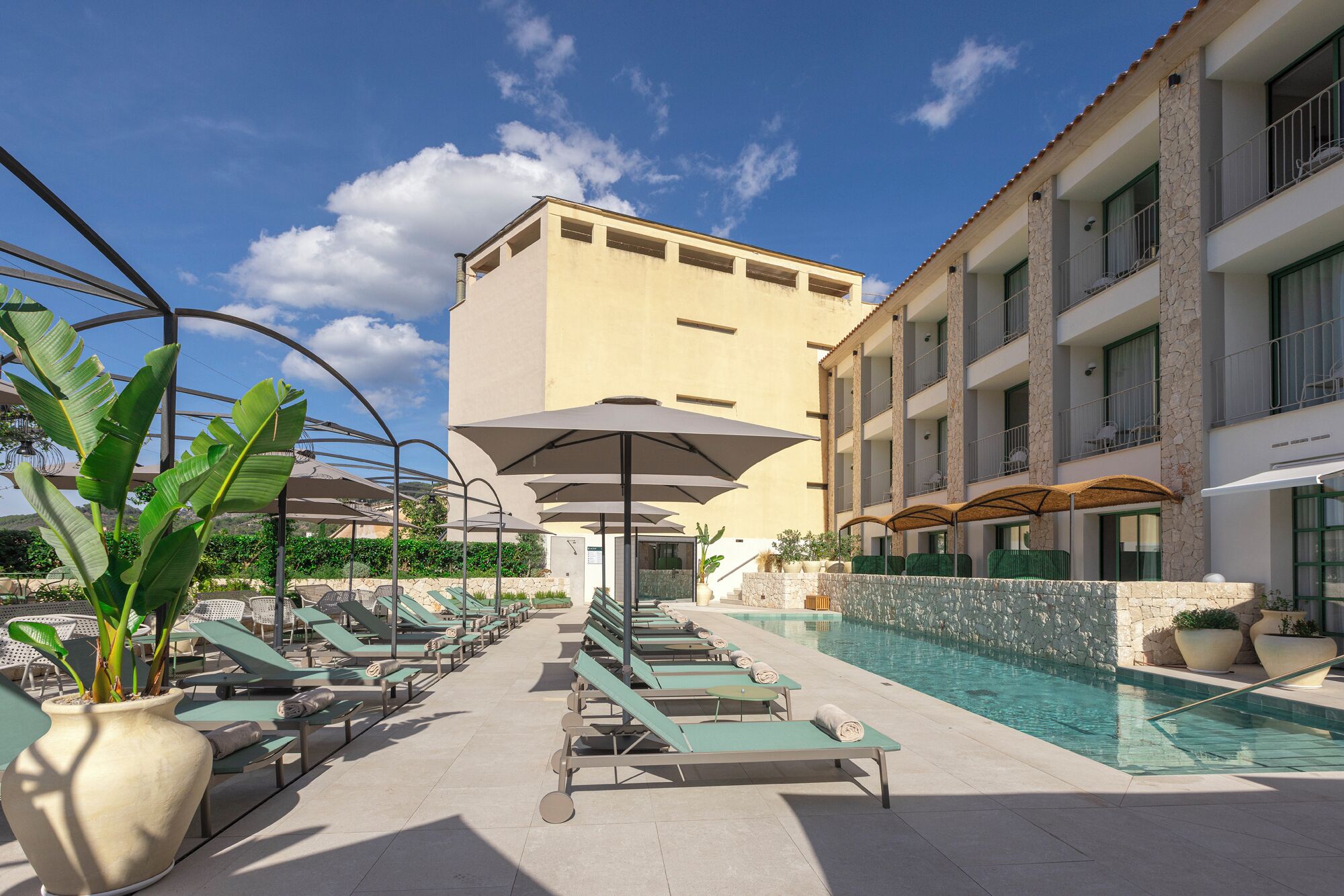Un área junto a la piscina con sillas de descanso y sombrillas, piscina y un edificio con balcones.