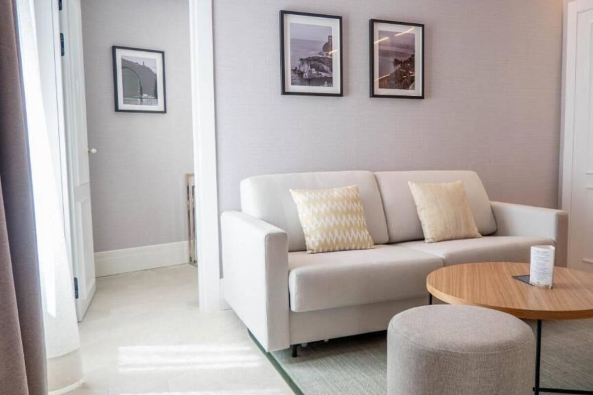 A modern living room with a sofa, two pillows, a round wooden table, and framed pictures on the wall.
