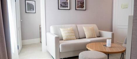 A modern living room with a sofa, two pillows, a round wooden table, and framed pictures on the wall.