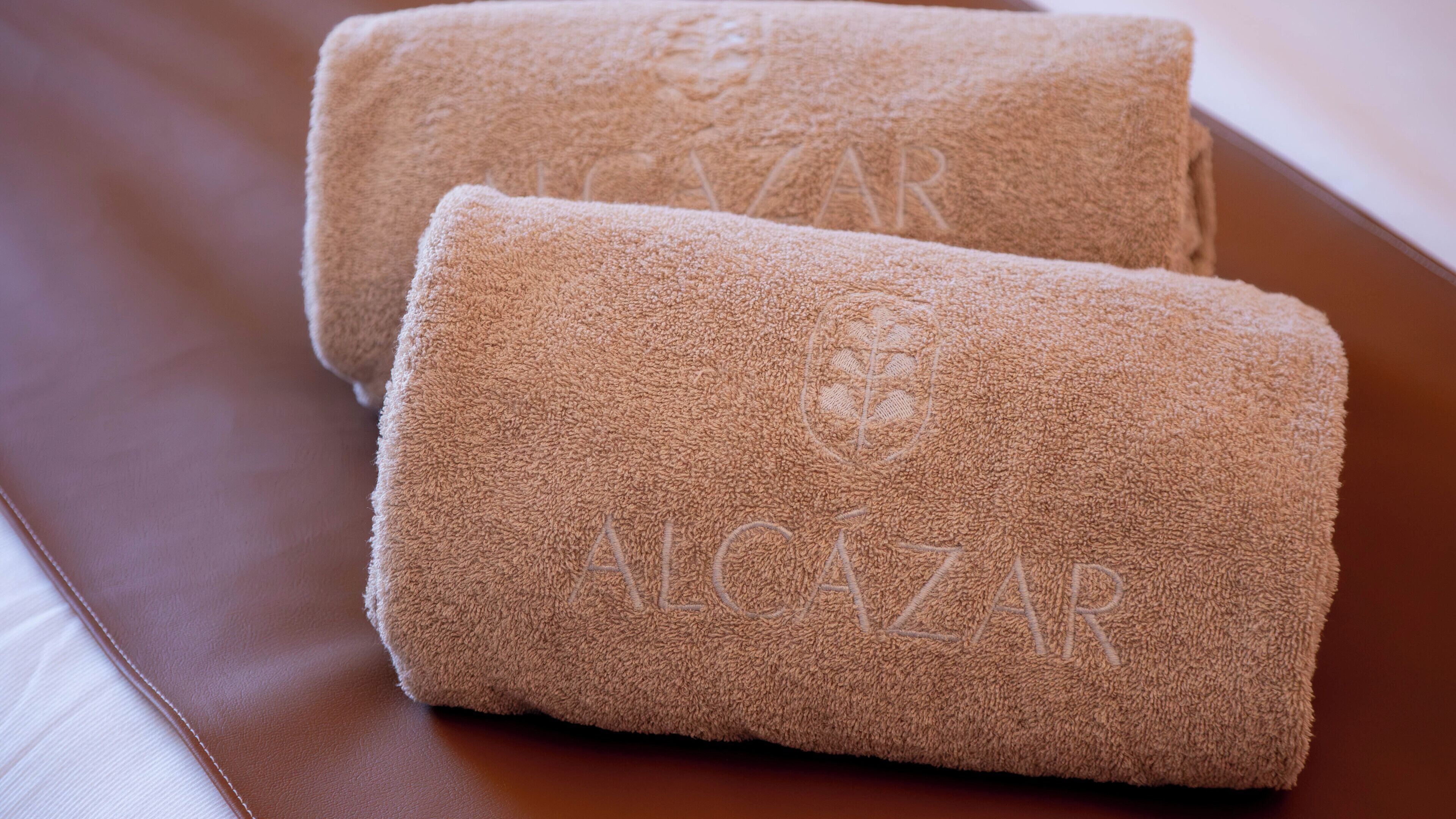Two rolled towels with the text "ALCazar" on a brown leather surface.
