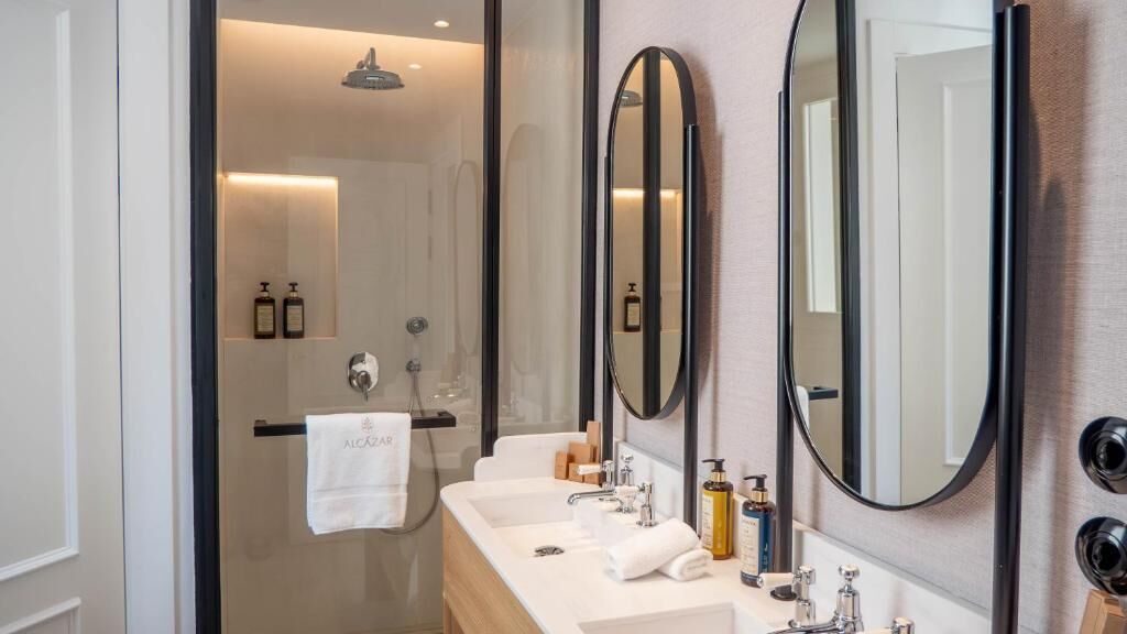 A modern bathroom with a glass shower enclosure, a double sink vanity, and two large mirrors.