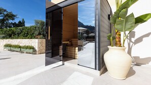A modern building entrance with a glass door, outdoor seating, and a large potted plant. - Alcázar Hotel Sóller (Sóller)