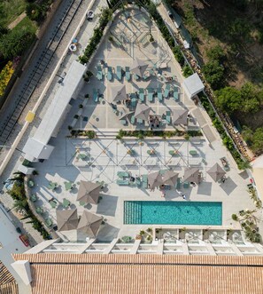 Vista aérea de un complejo turístico con piscina, zonas de estar al aire libre y una vía de tren cerca.