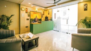 A reception area with a green counter, two leather sofas, a coffee table, and a ceiling fan. - Treebo Elite Corporate, Sector 62 (New Delhi)