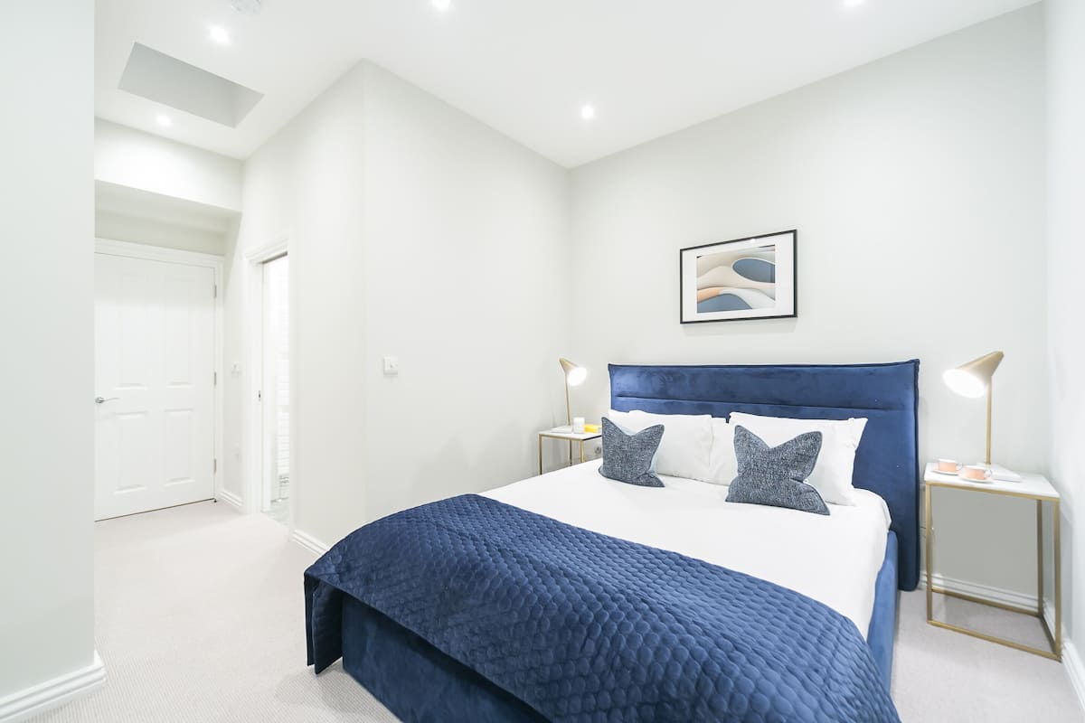 Une chambre à coucher avec un grand lit, des murs blancs, une tête de lit bleue et un tableau encadré accroché au mur.