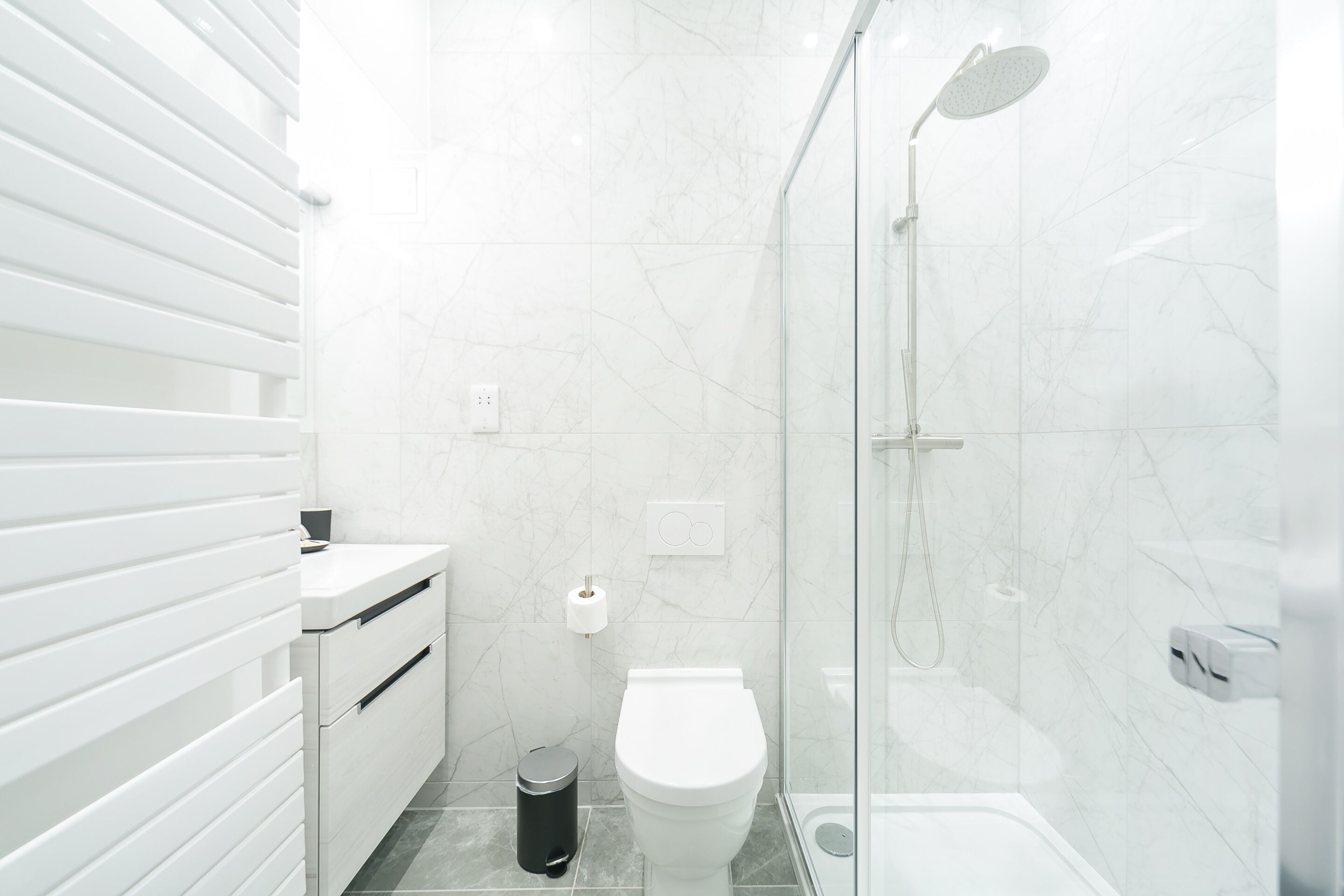 Un bagno moderno con box doccia in vetro, un water bianco e un cestino.