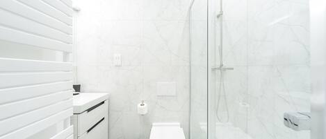 Un bagno moderno con box doccia in vetro, un water bianco e un cestino.