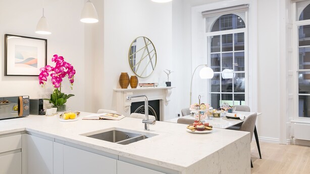 A modern kitchen with a marble countertop, a built-in sink, pendant lighting, and a dining area with a table set for a meal. - Urban Chic - Acre (London)