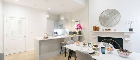 A modern kitchen with white cabinetry, a central island with bar stools, and a dining area with a white table and chairs.