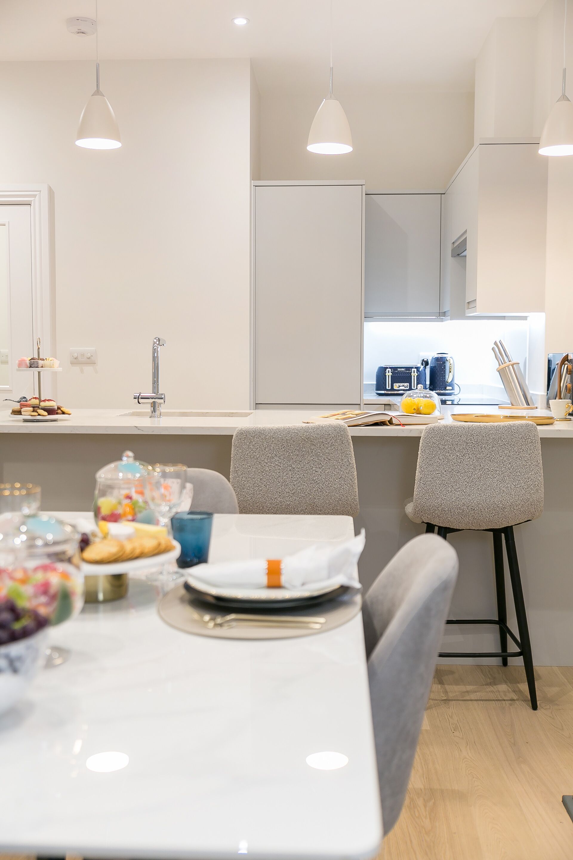 A modern kitchen with a white countertop, two pendant lights, and a window with kitchen appliances.