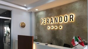 A reception desk with a name sign 'PERANDOR' and a clock. There are flags and a small plant on the desk. - Perandor Beach Hotel (Durrës)