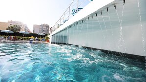 A pool area with clear water, a white structure with blue accents, and a few people in the background. - Perandor Beach Hotel (Durrës)