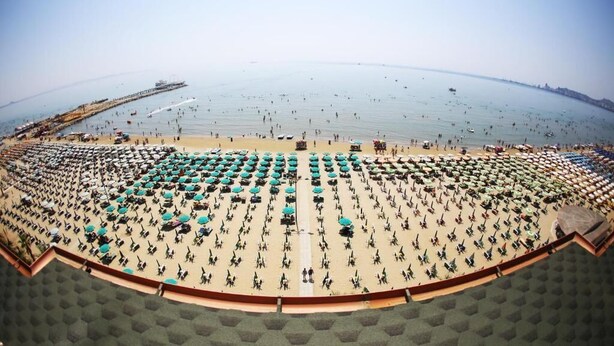 A beach with rows of umbrellas and chairs, a pier in the background, and the sea. - Perandor Beach Hotel (Durrës)
