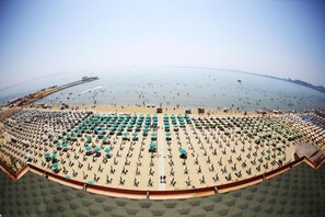 A beach with rows of umbrellas and chairs, a pier in the background, and the sea. - Perandor Beach Hotel (Durrës)