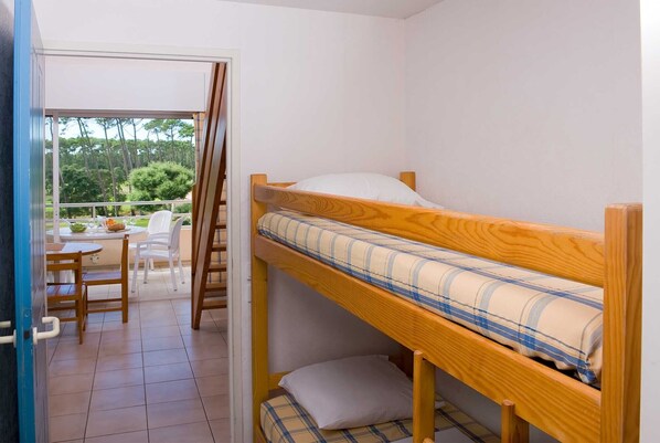 A small, single-bedded room with a wooden bunk bed, a small table with chairs, and a view of a garden through an open door. - Les Appartements de Moliets (Moliets-et-Maa)