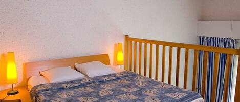 Un dormitorio con cama de madera, dos lámparas de noche, una colcha estampada y vistas de una cortina a rayas.