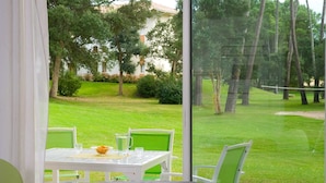 A dining table with chairs and a view of a grassy area with trees and a building in the background.