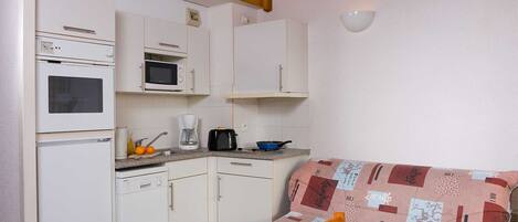 A compact kitchen with a microwave, oven, and coffee maker. There's a small dining area with a table and a cushion.