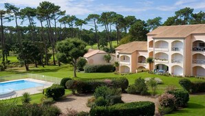 A hotel with a pool, surrounded by well-maintained gardens and tall trees.