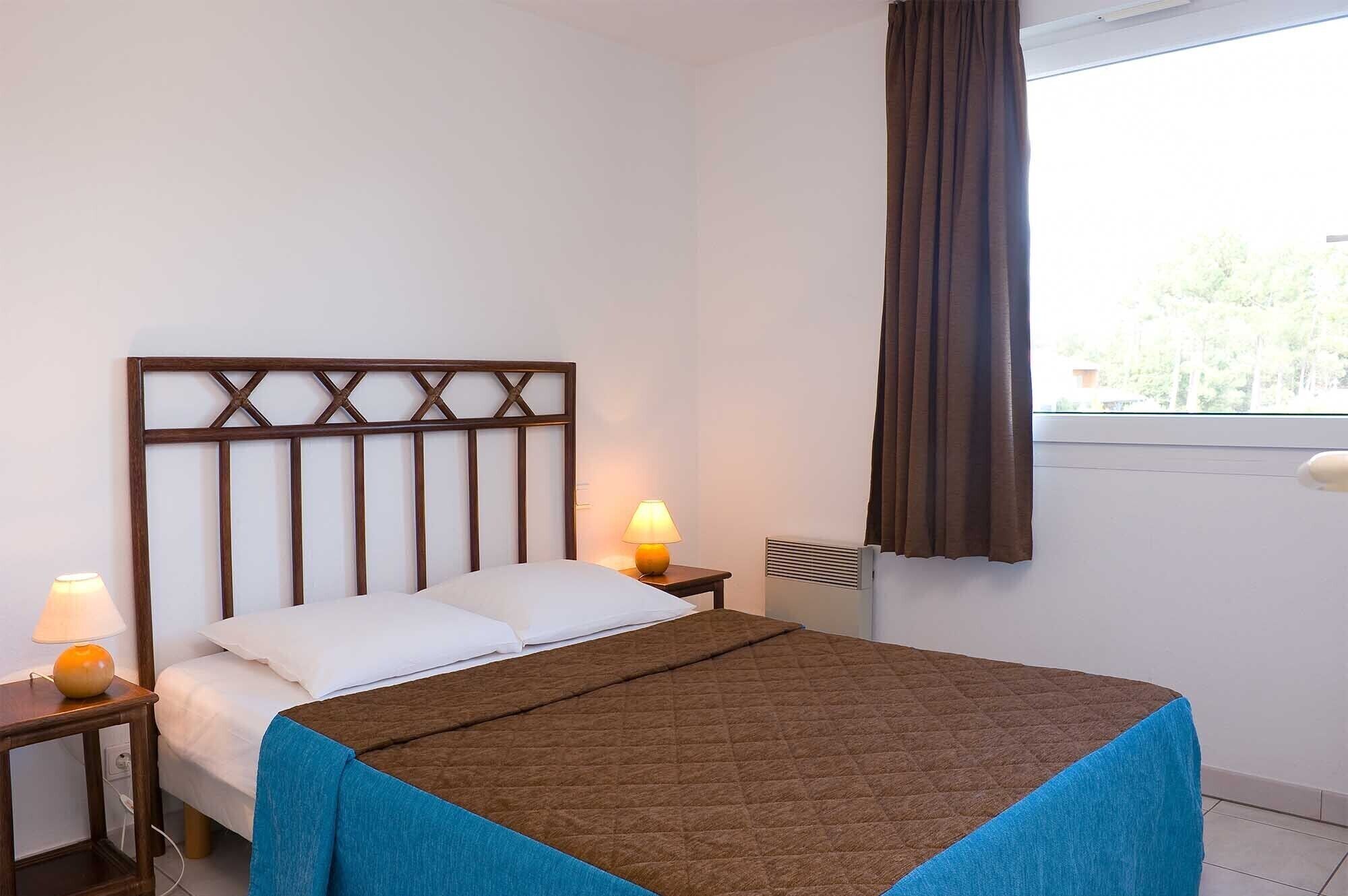Habitación de hotel con cama, mesita de noche, lámpara, ventana con cortinas y radiador.