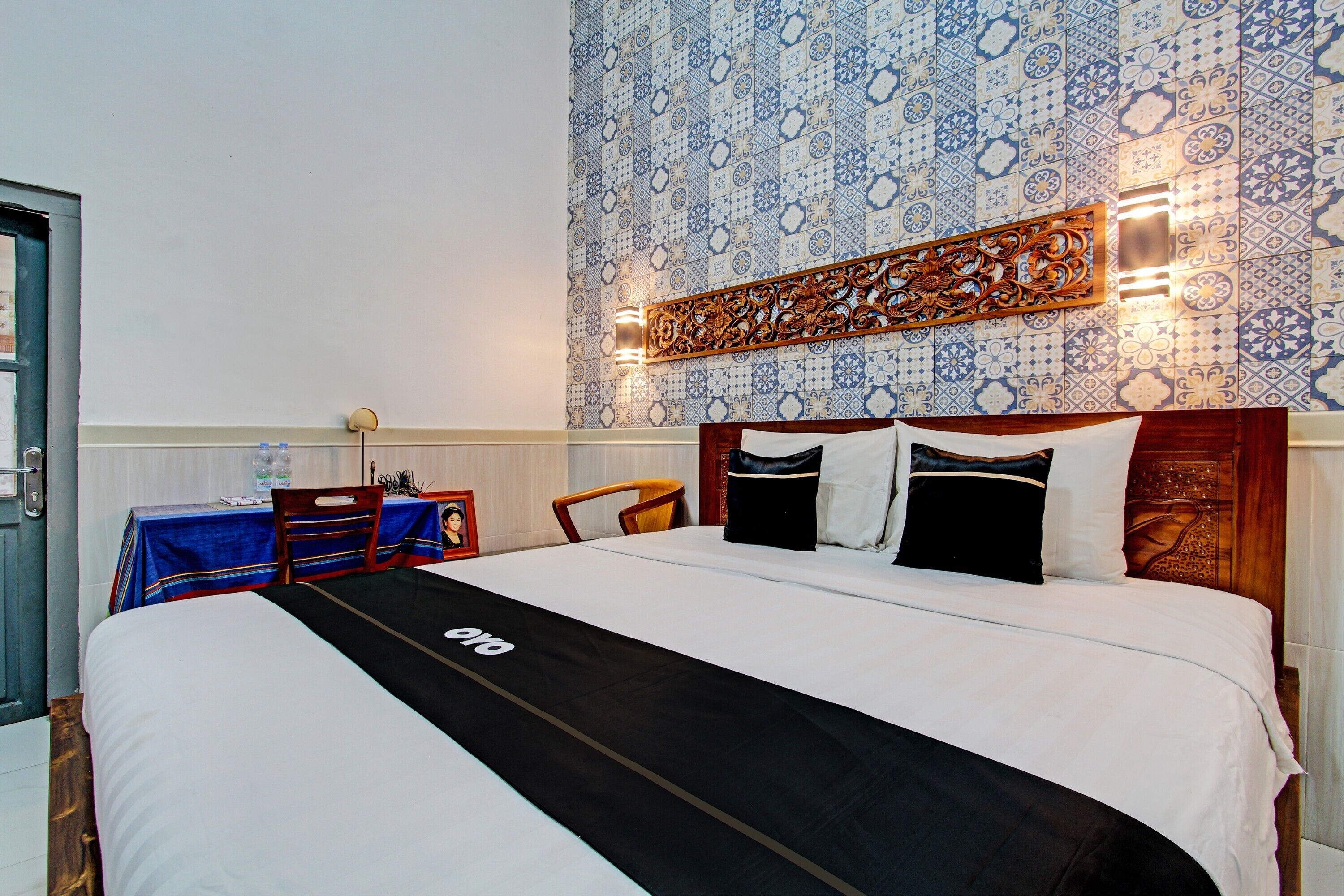 A hotel room with a large bed, a desk with a chair, and a patterned wall.