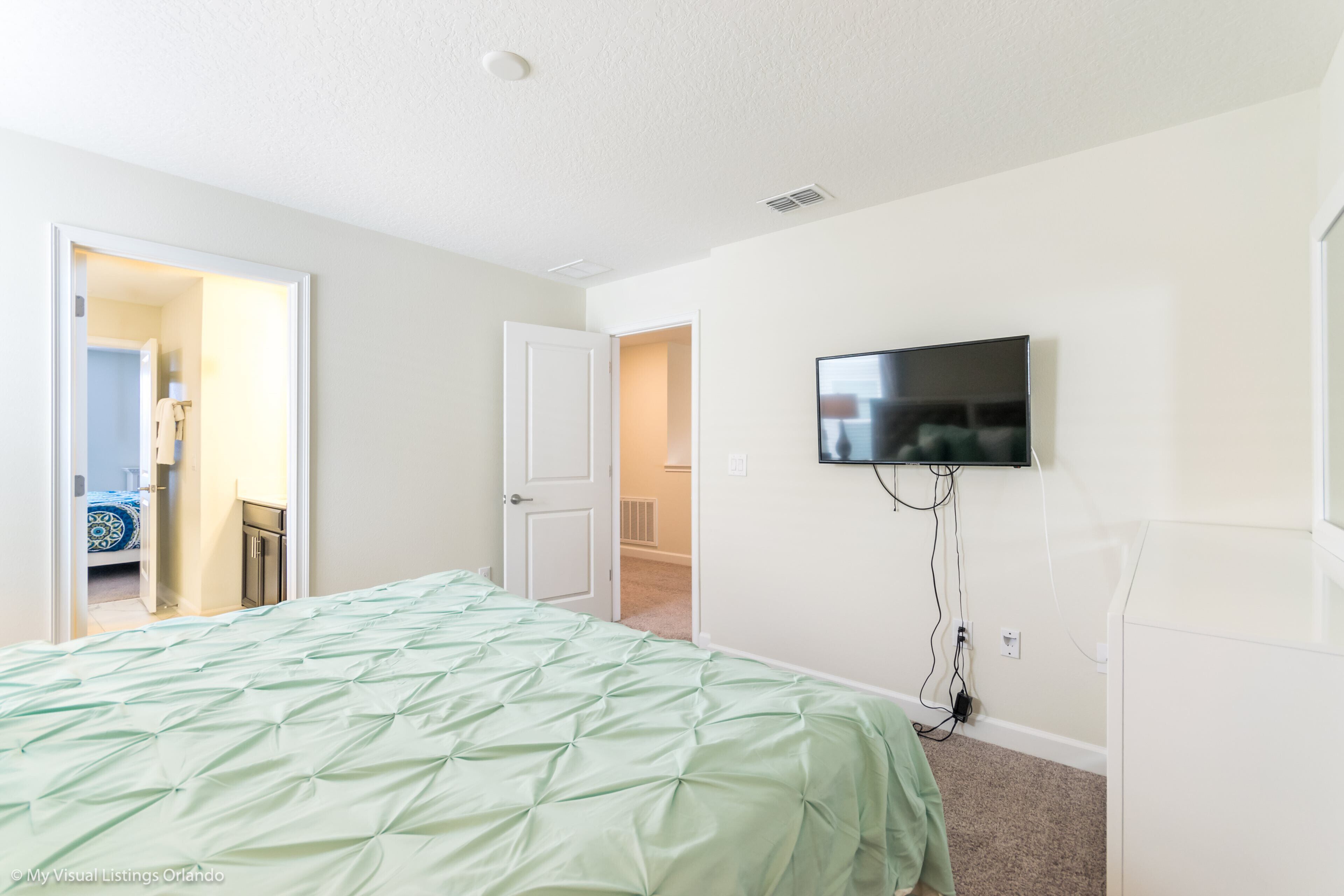 A bedroom with a bed, a television mounted on the wall, and a door leading to another room.
