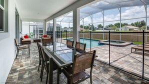 Un portico coperto con tavolo e sedie in vetro, una piscina e vista sulle case circostanti.